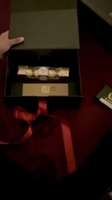 Hands opening the black presentation box to a gold-sealed scroll inside
