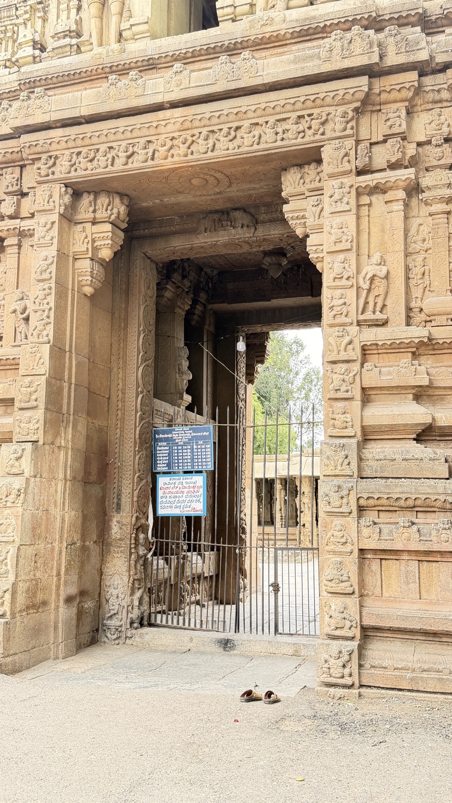 A deeply carved stone temple doorway, an iron gate half-open onto a sunlit courtyard, a single pair of slippers left on the ground outside.