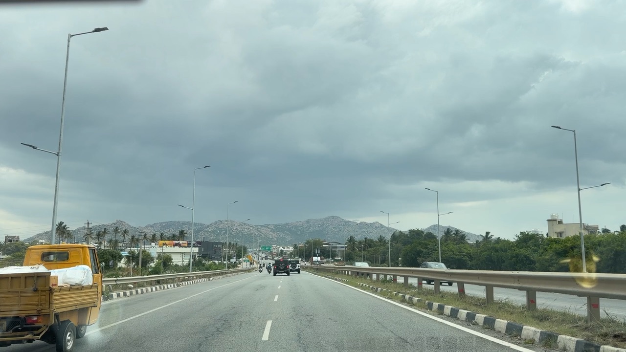 A view from a moving car on an open road heading toward low granite hills under a grey morning sky.